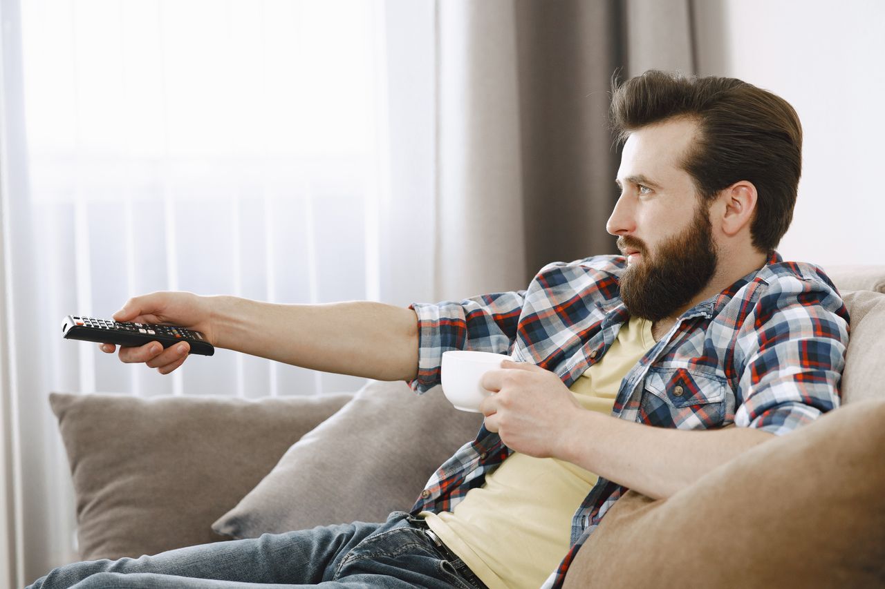 Person startar iptv med fjärrkontrollen i soffan